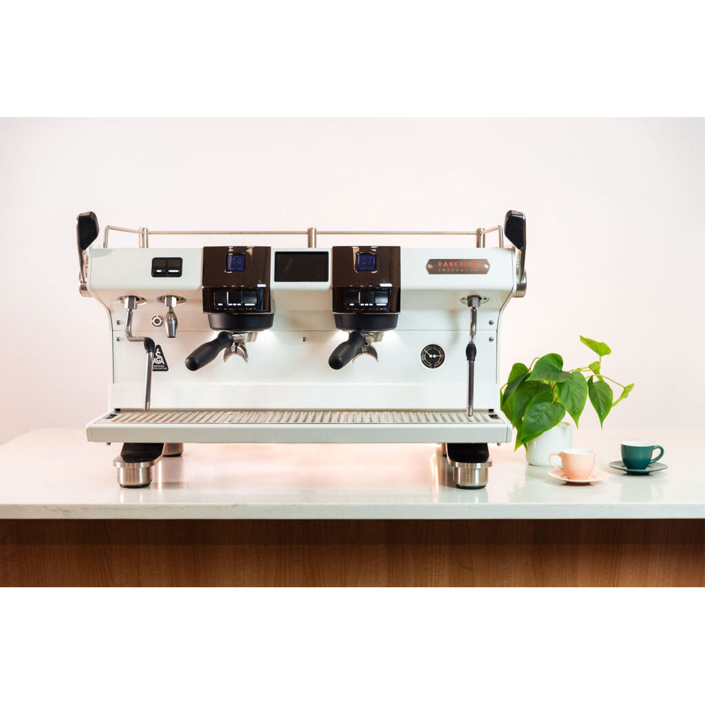 White Rancilio RS1 two group head espresso machine on bar with cups and plant